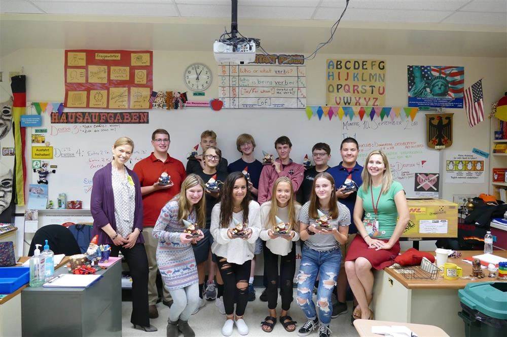 Students each holding a gnome and a teacher stand together. Students each holding a gnome and a teacher stand together.