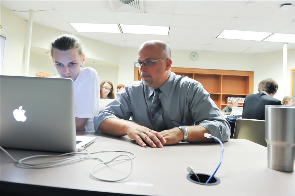Student and teacher sit together looking at a laptop.